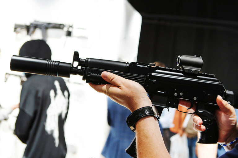 Firearms. Automatic machine gun with a silencer and an optical sight in the hands of a man. Close-up. Unrecognizable person