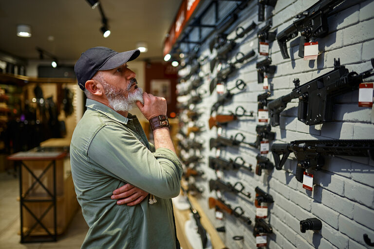 Male seller at showcase with rifles in gun store